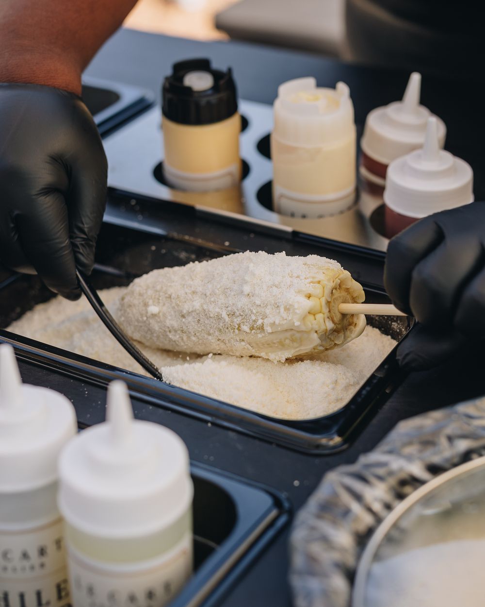 An elote on a stick being rolled in cotija cheese