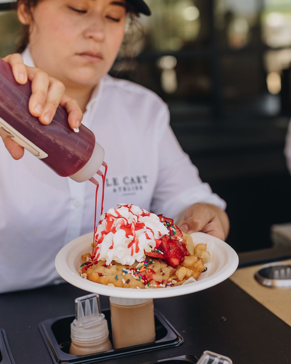 Strawberry sauce drizzled over a funnel cake topped with whipped cream and strawberries